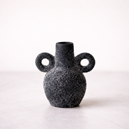 Black speckled vase with two circular handles on a white background