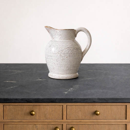White ceramic pitcher on a dark marble countertop with wooden cabinets in the background.