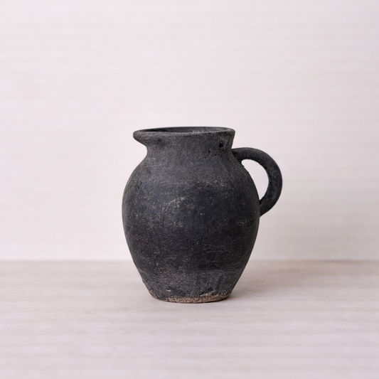 Black ceramic jar with a handle on a light gray background