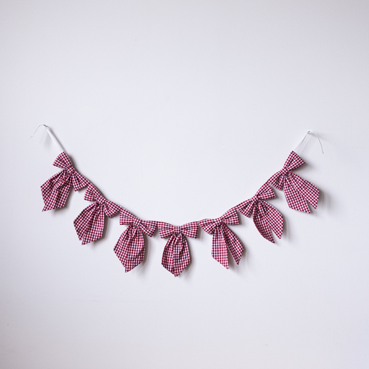 Red gingham fabric bow garland featuring multiple fabric bows on a string, perfect for decorative party or home decor.