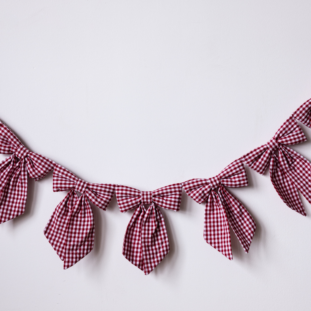 Red gingham fabric bow garland by Luxe B Co featuring multiple fabric bows on a string for decorative use.