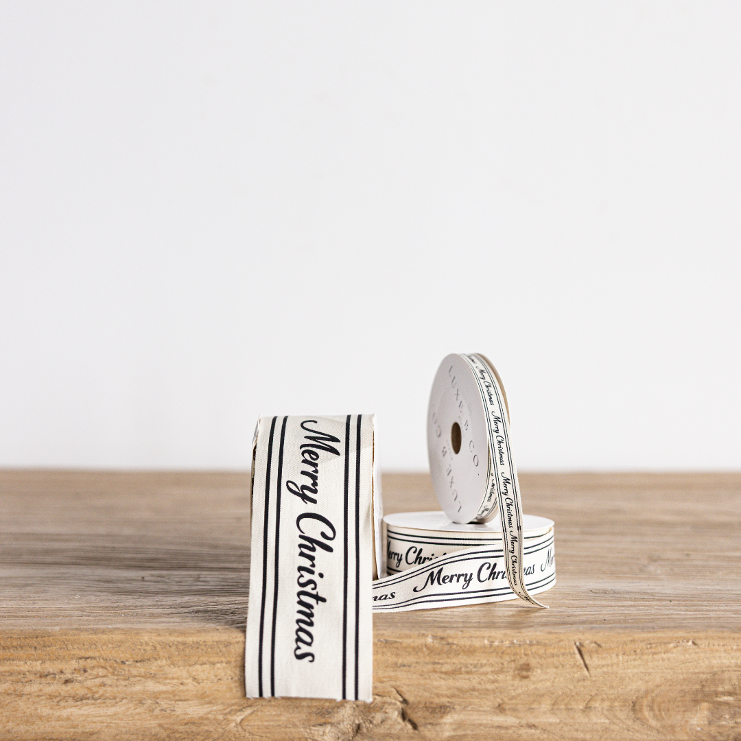 Black cursive writing Merry Christmas ribbon by Luxe B Co Wholesale, featuring elegant holiday-themed text on satin fabric.