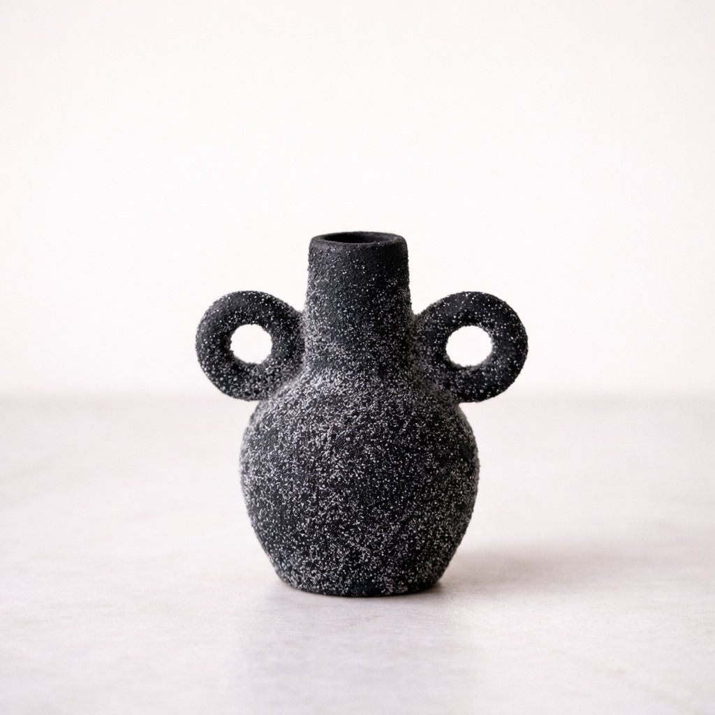Black speckled vase with two circular handles on a white background