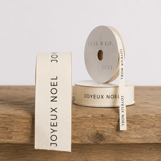 White woven ribbon with "Joyeux Noel" design by Luxe B Co, perfect for holiday gift wrapping or festive decorations.