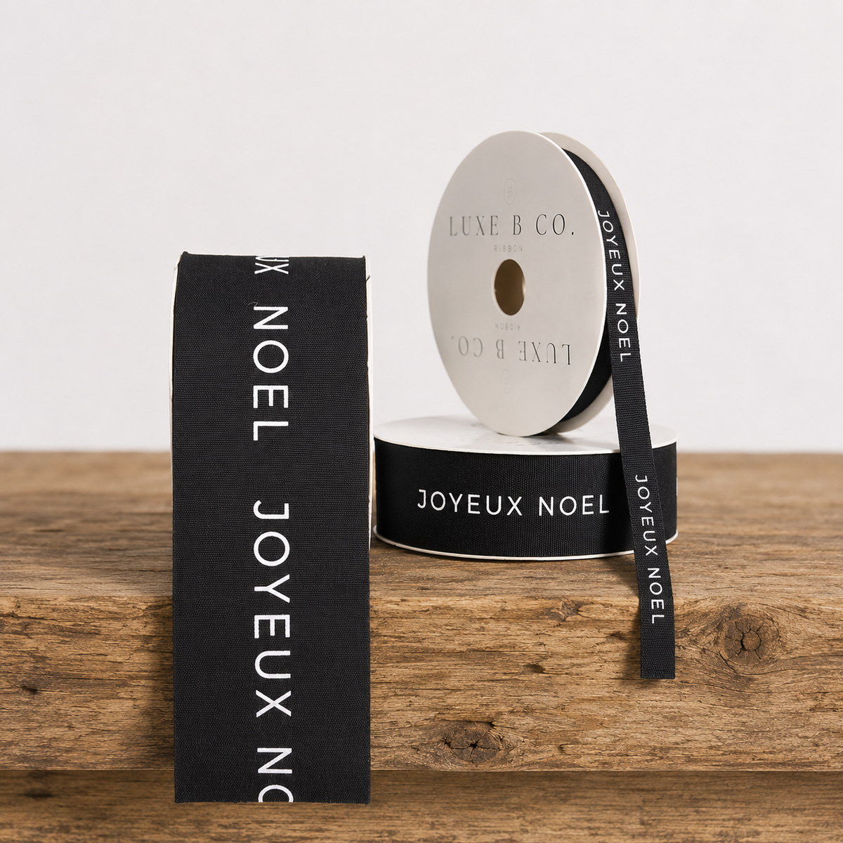 Black woven ribbon with "Joyeux Noel" text from Luxe B Co, perfect for holiday decorations or gift wrapping.