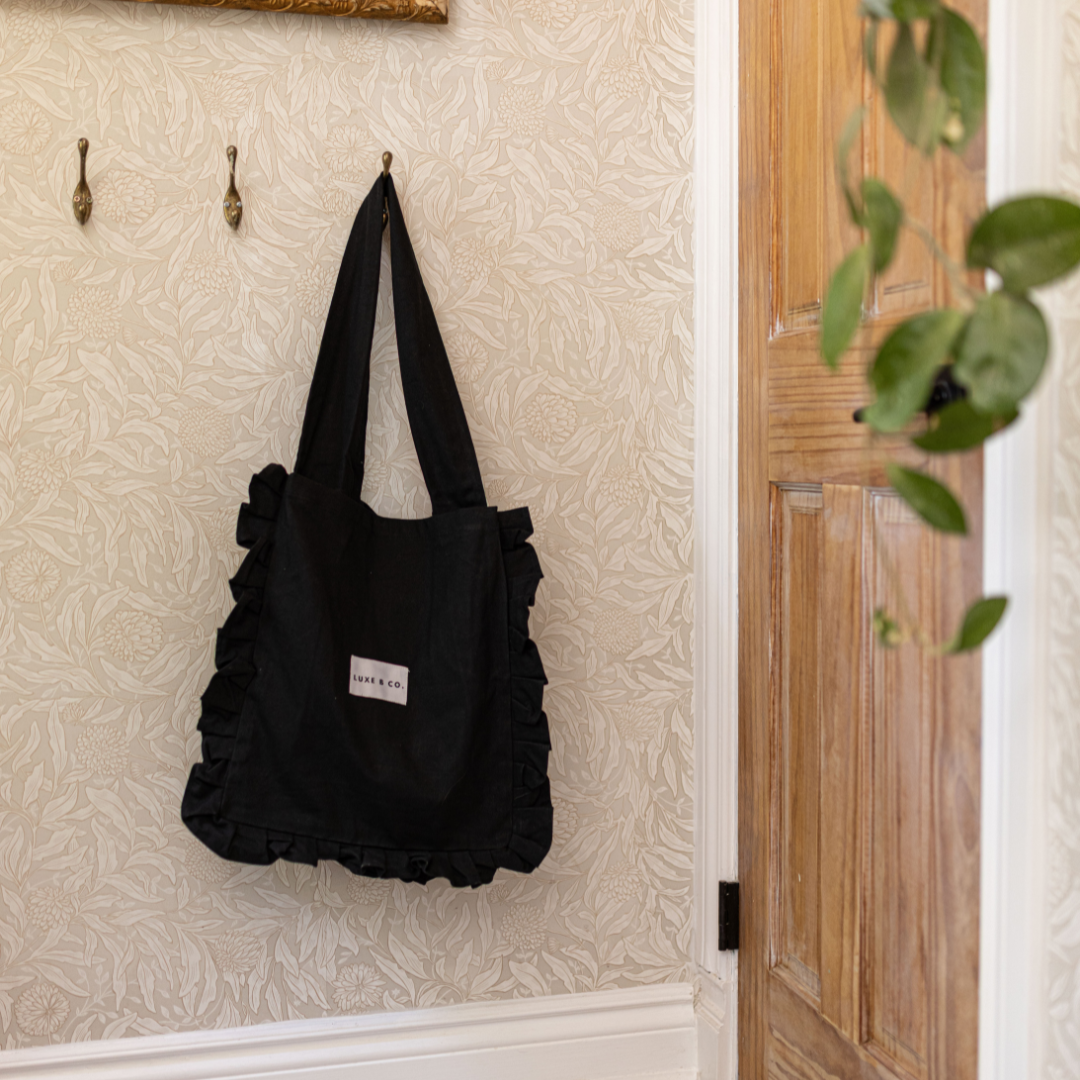 Black Luxe B Co. tote bag with ruffle detailing, made of stylish fabric, featuring sturdy handles and a spacious interior.