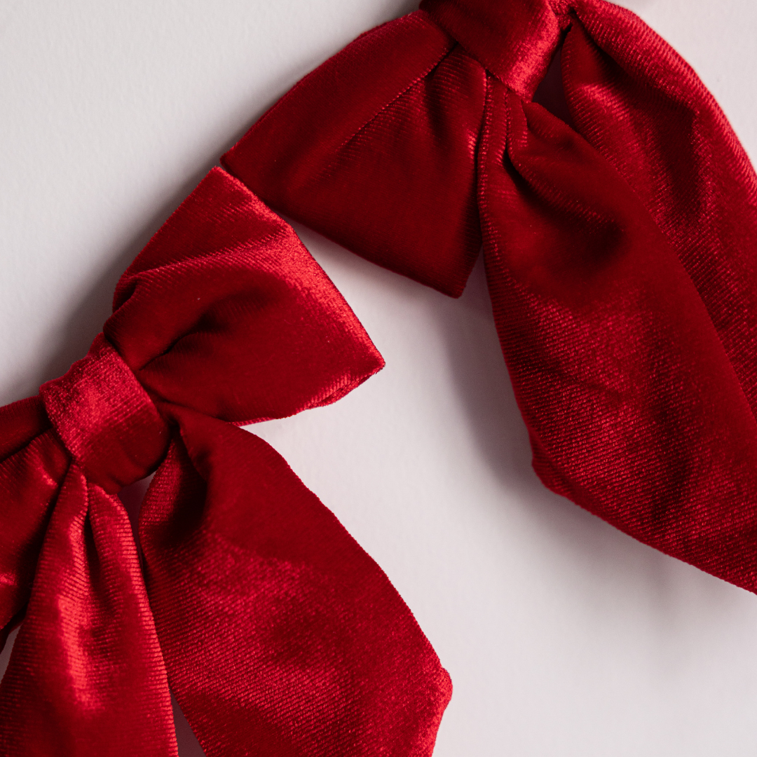 Red velvet fabric bows on a garland, styled by Luxe B Co, perfect for elegant decoration or festive events.