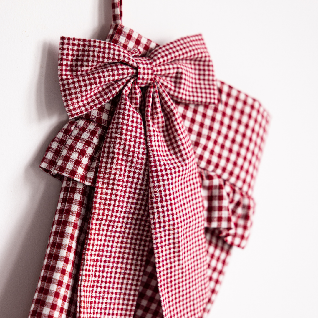 Red gingham holiday stocking with a bow by Luxe B Co, featuring festive red and white checkered fabric and decorative bow detail.