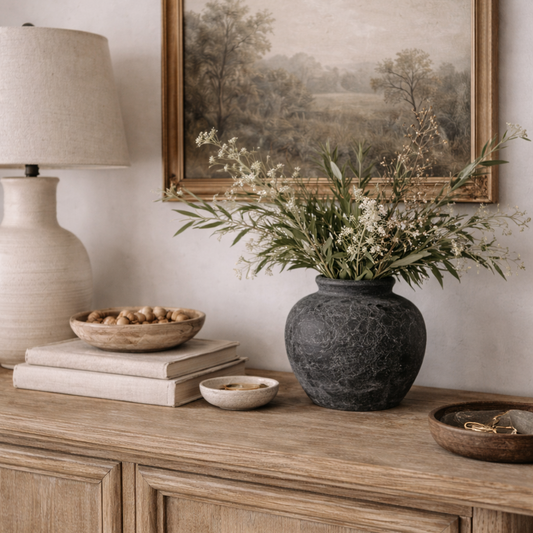 Wooden sideboard with decorative items including a vase of flowers, books, and a lamp.