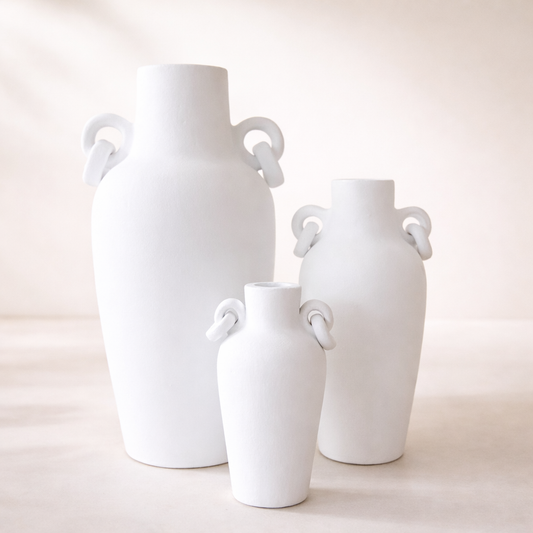 Three white ceramic vases with handles on a light beige background