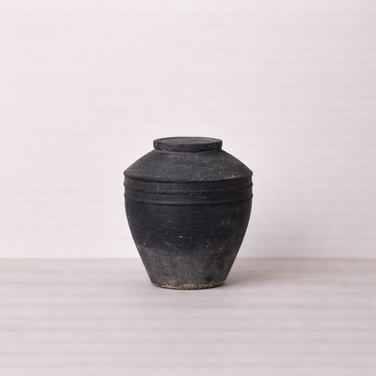 Black ceramic jar with lid on a light gray background